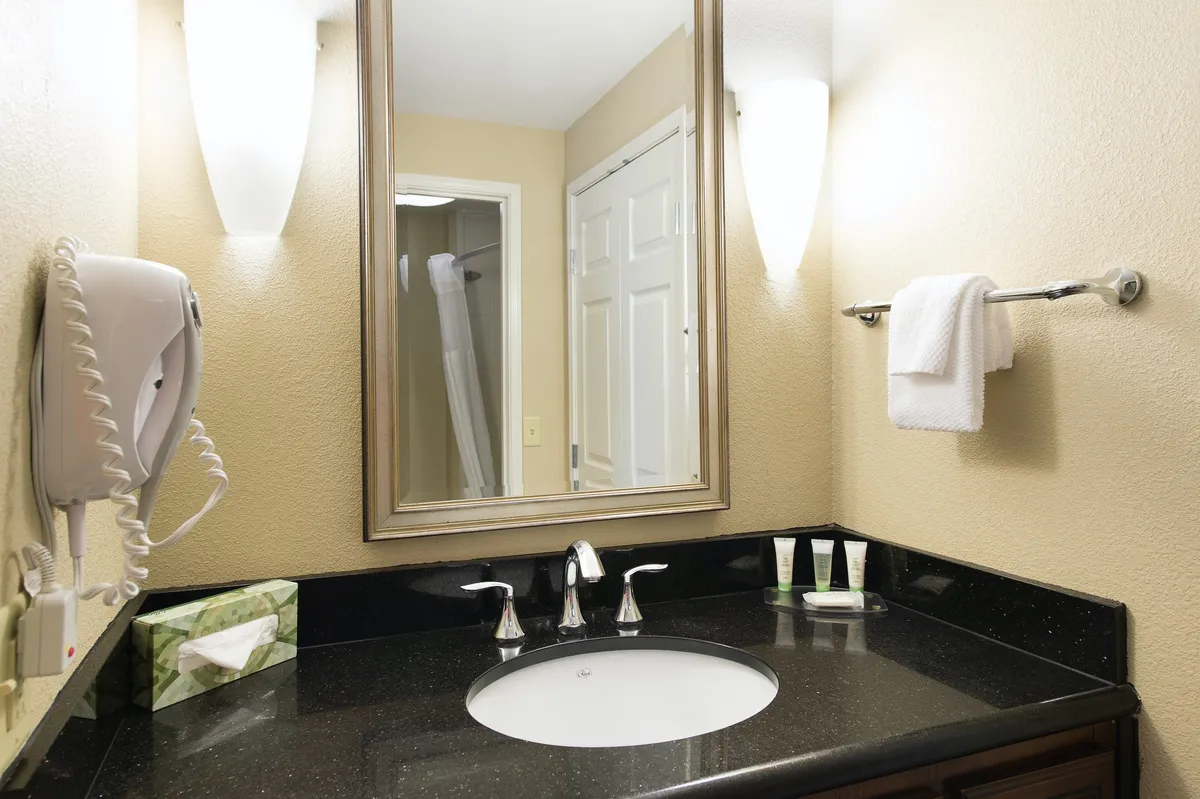 A modern, well-lit bathroom with a large mirror, stylish sink, ample countertop space, and neatly arranged fresh towels. Thoughtful lighting and organized amenities, including a visible hairdryer, create a sense of convenience and comfort.