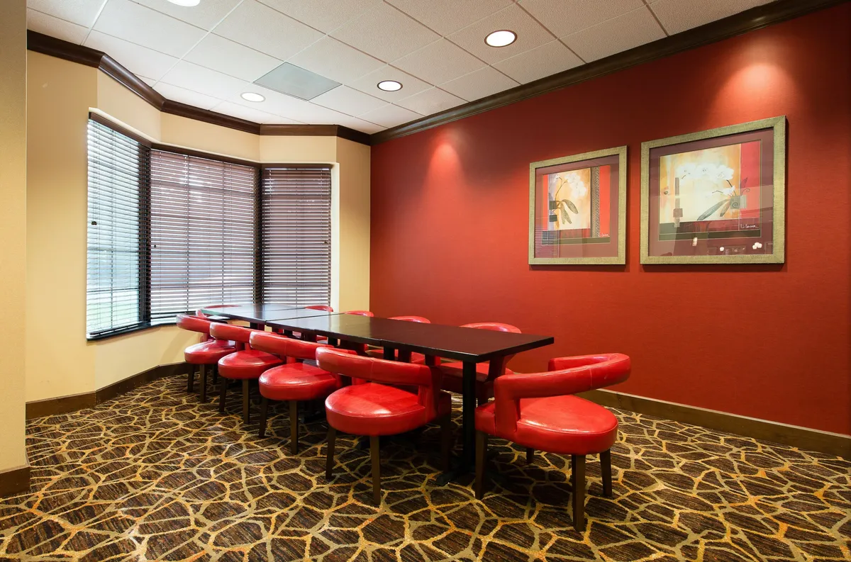 A dining space featuring a long table surrounded by red chairs, complemented by modern artwork on the walls. The ambiance is casual yet stylish, perfect for business meetings, family gatherings, or shared meals.