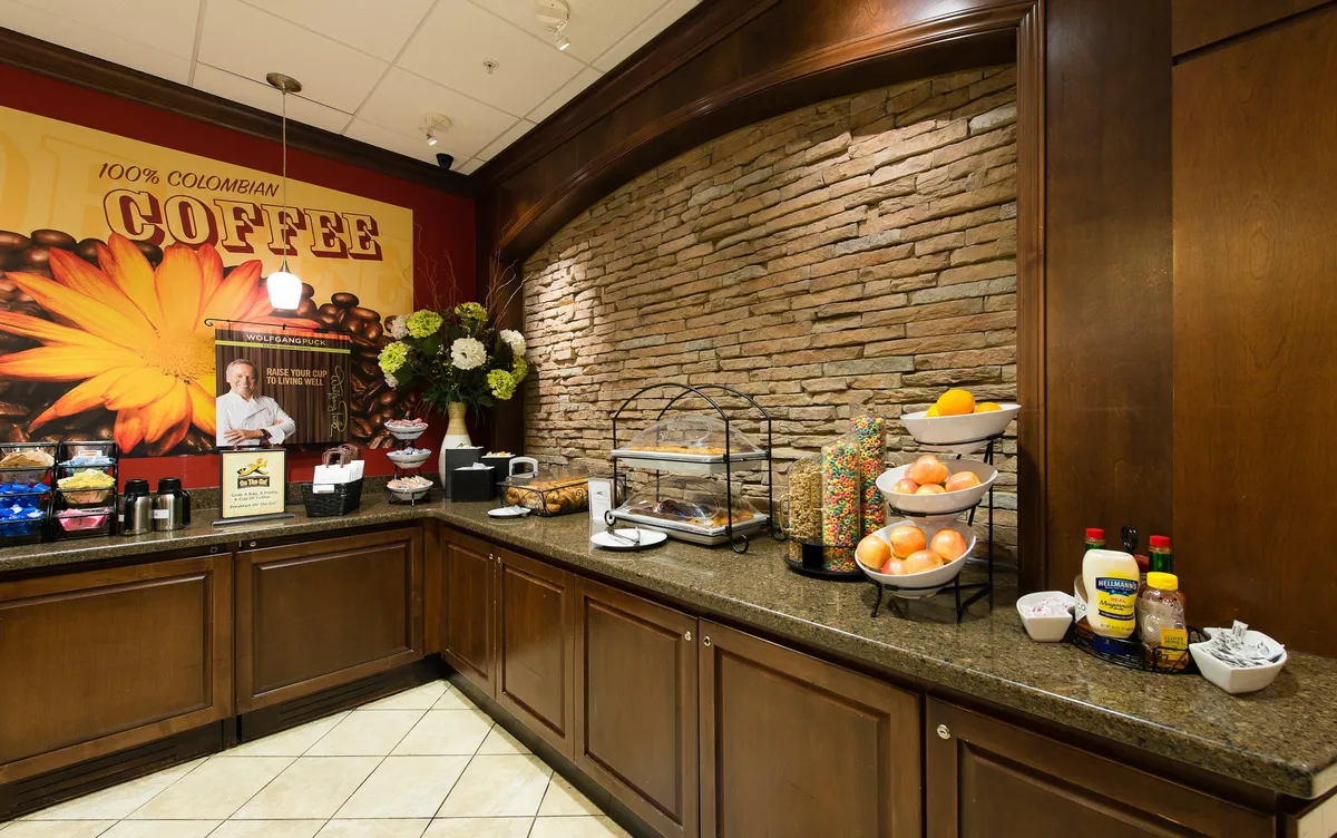 A welcoming coffee station and snack display set against a decorative wall, complete with a fruit basket and comfortable seating area. The inviting ambiance encourages guests to relax, socialize, and rejuvenate throughout their stay.