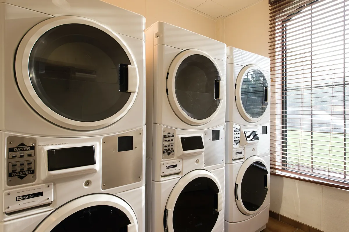 This interior image focuses on the laundry facilities, with a row of washing machines and dryers set against a window with blinds. The space is clean, organized, and practical, perfectly illustrating the convenience offered to guests.