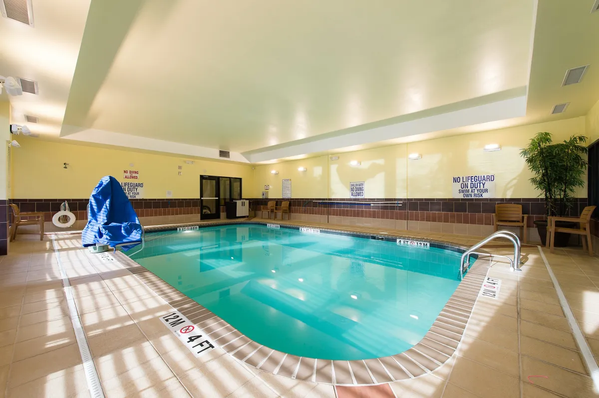 A bright, well-lit indoor swimming pool surrounded by comfortable chairs, potted plants, and a relaxing ambiance. The pool area offers ample space for families to unwind, swim, or simply enjoy a laid-back afternoon.