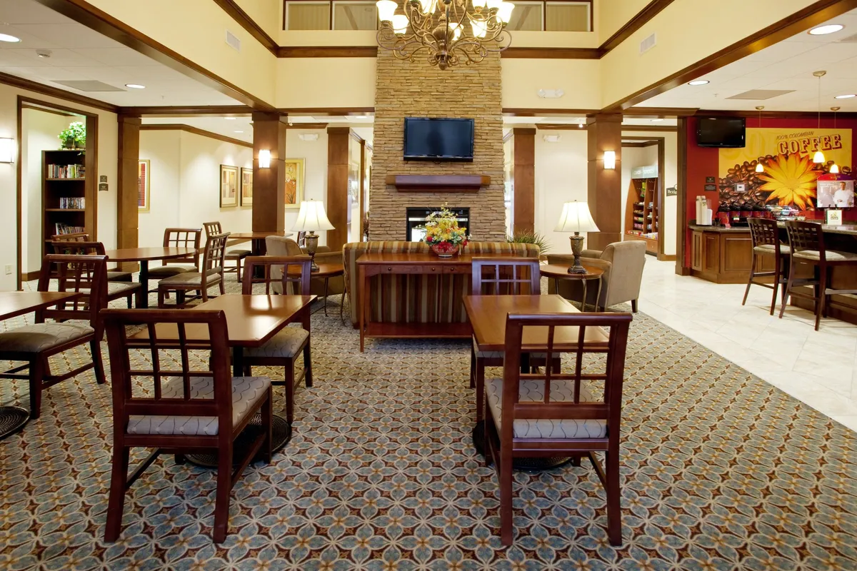 A cozy lounge area featuring a striking stone fireplace, elegant chandelier, mounted television, and an accessible coffee bar. The space invites guests to gather, relax, and share stories after a busy day exploring Columbia's attractions.