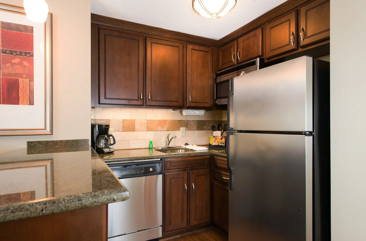 This image captures a kitchen and dining area featuring a spacious granite countertop, stainless steel appliances, and dark wooden cabinets. The space is inviting, with room for meal preparation and casual socializing, and suggests the ability to host anything from family breakfasts to dinner parties.